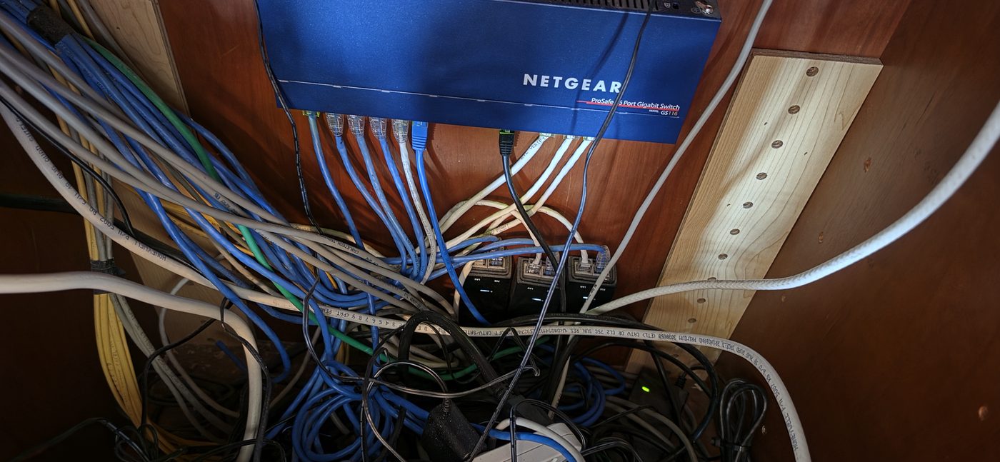 Tangled AV wiring and network switch inside a home equipment cabinet before cleanup