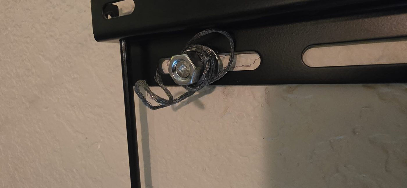 A TV mount bolt with a piece of wire wrapped around it in place of a washer, a failed installation behind a wall-mounted television