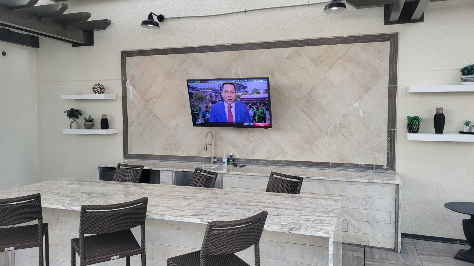 Covered rooftop outdoor kitchen with a wall mounted TV in indirect light