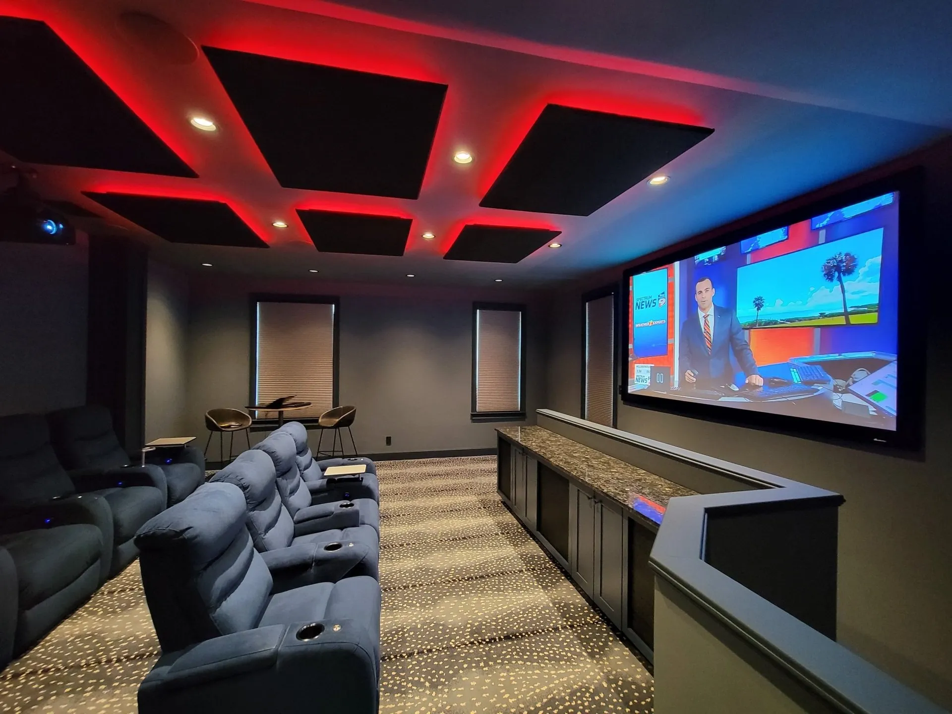 Dedicated home theater with red LED coffered ceiling, blue theater recliners, and large display