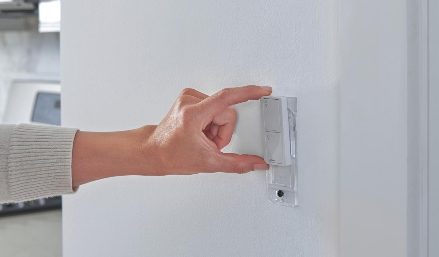 Hand pressing a Lutron Caseta Pico dimmer on a clean white wall