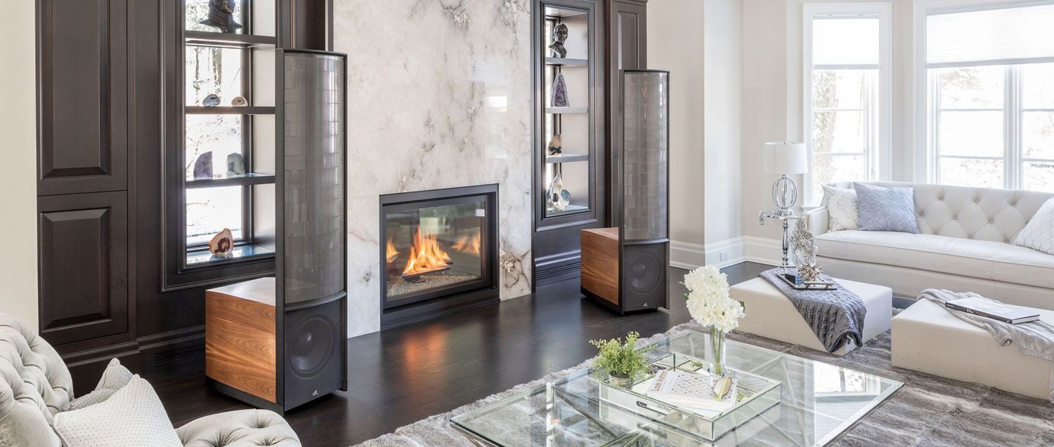 A pair of MartinLogan electrostatic speakers either side of a fireplace in a bright living room, with the sofas facing them