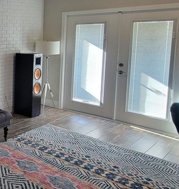A floorstanding tower speaker beside a floor lamp and French doors in a bright living room with a patterned rug