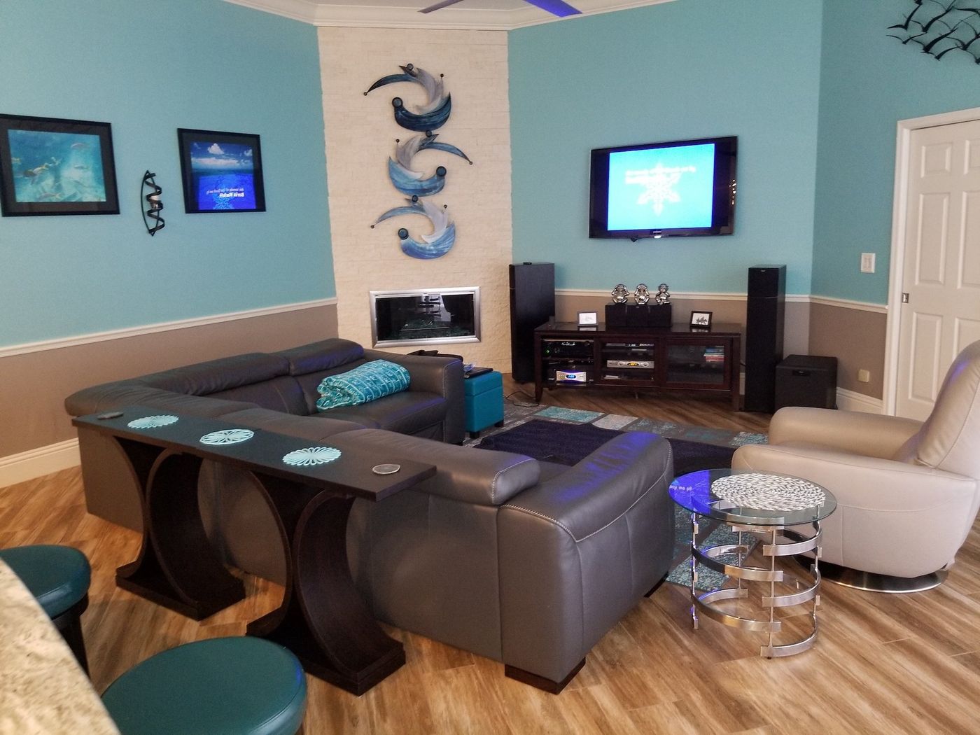 Floorstanding tower speakers either side of a media console below a wall mounted TV in a teal living room